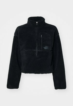 Svart fleece-pullover-jakke med høy krage, halv glidelås foran og brystlomme. Teksturert stoff og brodert logo på lommen.
