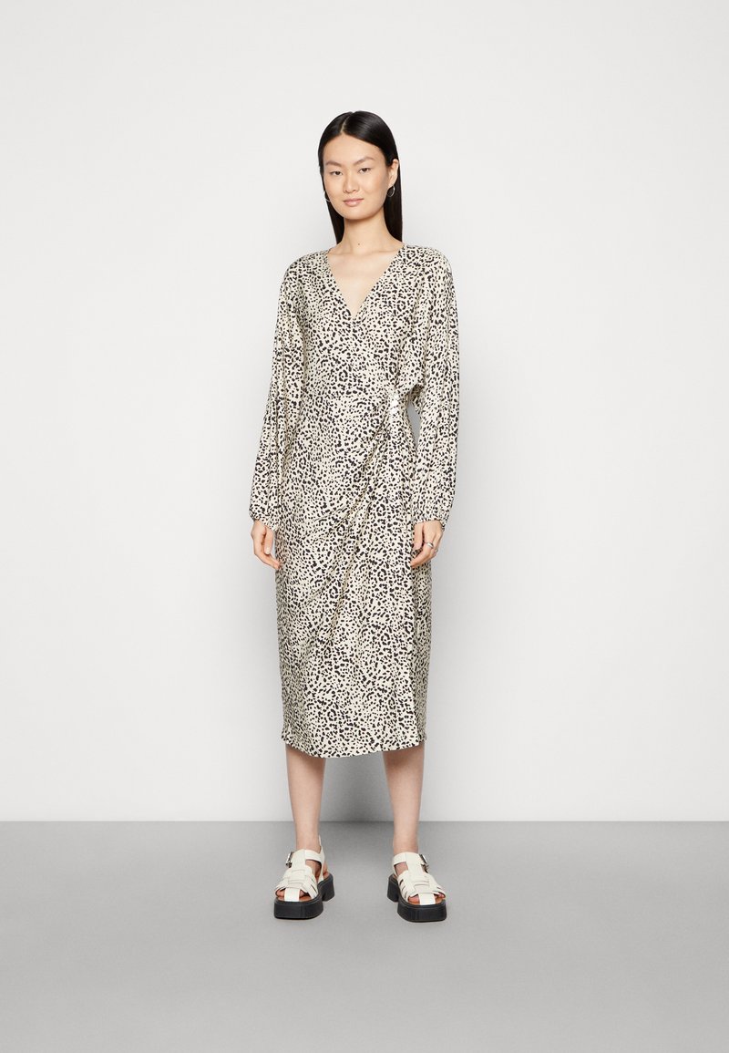 Vestido envolvente de estampa de leopardo com mangas longas, decote em V e detalhe de laço na cintura, feito de tecido leve. Combinado com sandálias de plataforma bege.