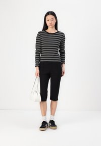 Svart og hvit stripete langermet topp, svarte cropped bukser, svarte sneakers med lyse såler, hvit håndveske, grå sokker, glatt tekstur.