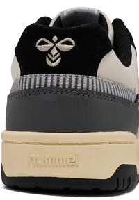 Tenisice s crnom sueded petom, sivom kožnom bazom i teksturiranim gornjim dijelom. Istaknuti crno-bijeli izvezeni logo pčele. Hummel branding na srednjem sloju.