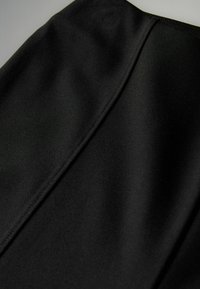 Tela negra con una textura suave, que presenta un detalle de costura prominente. El material parece flexible y mate, sin patrones ni hardware visibles.