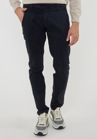 Chino navy in cotone, vestibilità slim, con tasche frontali, chiusura a bottone e una texture discreta. Abbinati a sneakers grigie e bianche.