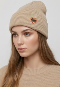 Beige knitted beanie with ribbed texture, featuring a heart-shaped leopard print patch outlined in orange.