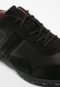 Basket noire avec une combinaison de cuir lisse et de daim, ornée de surpiqûres roses et d'un panneau en maille à la languette pour une meilleure respirabilité.