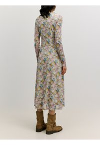 Blumendruckkleid mit langen Ärmeln, aus leichtem Stoff gefertigt. Verfügt über ein tailliertes Oberteil und einen schwingenden Rock, kombiniert mit braunen Knöchelstiefeln.