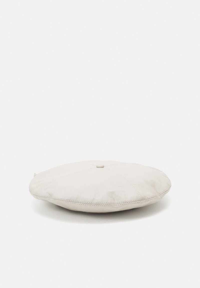 Kulatý krémově zbarvený kožený polštář s prošívaným vzorem a středovým knoflíkem. Hladký povrch, plochý tvar, minimalistický design.