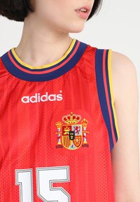 Maillot de basketball rouge avec texture en maille, col rayé bleu et jaune, logo brodé de l'Espagne et numéro 15 blanc sur le devant.
