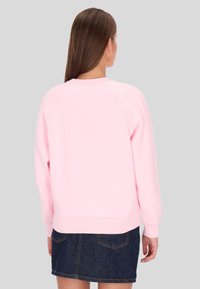 Sudadera rosa con cuello redondo y mangas raglán, combinada con una falda de mezclilla oscura. Textura suave y puños acanalados.