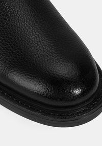 Zwarte leren dressboot met een gestructureerde afwerking, ronde neus en een glad, gepolijst oppervlak. Voorzien van een gestikte zool voor duurzaamheid.