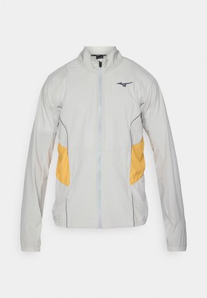 Helle graue Jacke mit gelben seitlichen Akzenten, Reißverschluss, Stehkragen und elastischen Bündchen. Hergestellt aus einem glatten, leichten Stoff.
