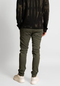 Svart tie-dye långärmad topp med olivgrön tapered byxor och ljusa sneakers. Tyget är bomull med en slät yta.