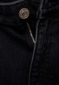 Schwarze Jeans aus Denim mit einem metallenen Knopfverschluss und Reißverschluss. Die Stoffstruktur ist glatt mit einem leichten Glanz und hat kontrastierende Nähte.