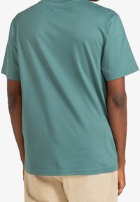 Camiseta de manga corta en suave algodón color teal, con cuello redondo y dobladillo recto. Diseño simple y sin adornos con una textura suave.