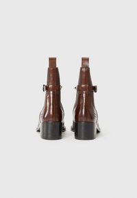Bottines en cuir marron avec une finition lisse, panneaux latéraux élastiques, tirant à l'arrière et talon carré. Détail de logo estampé près du talon.