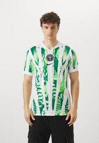 Maillot de football blanc avec des motifs de feuilles abstraites vertes, design en V, avec un emblème circulaire noir et le logo Nike sur la poitrine.