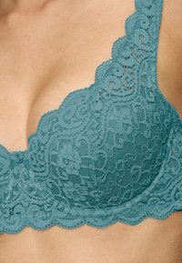 Teal blonde med blonder, blomstermønstre, bølgete kanter og en glatt tekstur. Stropperne er brede og intrikat utformet.