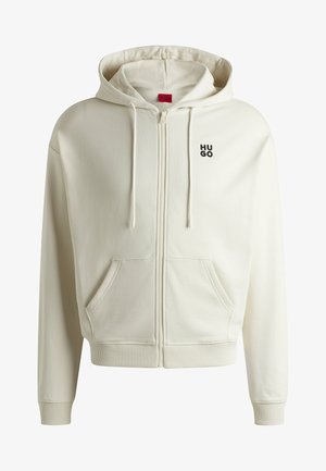 Haut de sweat zippé crème en tissu doux, présentant une poche avant, des poignets et un ourlet côtelés, et un logo noir "HUGO" sur la poitrine.