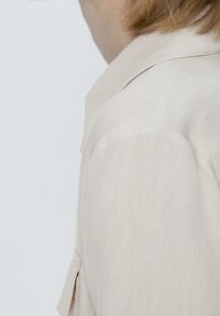 Hellbeige Leinenblazer mit strukturiertem Kragen und seitlichen Taschen. Besitzt einen strukturierten Stoff und eine maßgeschneiderte Passform.