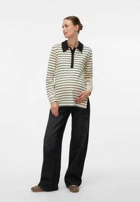 Polo premaman a maniche lunghe a righe in crema con righe nere e colletto, abbinato a pantaloni in denim scuro a gamba larga e scarpe marroni.