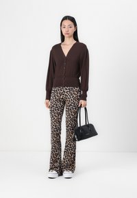 Brun cardigan med V-hals og knappelukking, kombinert med leopardmønstrede bukser med vide ben. Holder en liten svart håndveske. Hvite joggesko.