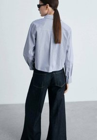 Relaxed-fit blue and white striped shirt with long sleeves, and dark denim wide-leg pants. Plain design, no visible patterns or accents.