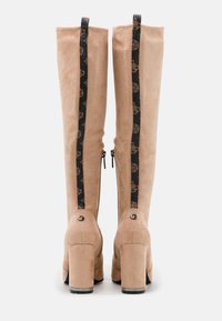 Bottes en suède beige jusqu'aux genoux avec une fermeture éclair noire arborant un motif de logo, des talons carrés et une finition texturée.
