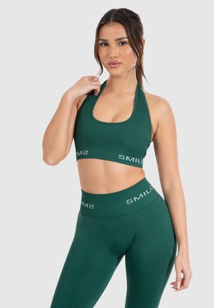 Dunkelgrüner Sport-BH und passende Leggings in gerippter Textur, mit einem Halterneck-Design und elastischen Taillengummis mit "SMILOS"-Branding.