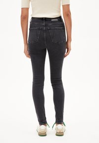 Jean skinny taille haute en denim gris foncé avec poches arrière, texture lisse et silhouette ajustée, assortis à des baskets beiges.