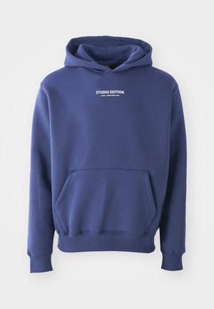 Tumši zili džemperis, izgatavots no mīksta auduma, ar kangaroo tipa kabatu, ribotām piedurknēm un uzrakstu "STUDIO EDITION" baltā krāsā pāri krūtīm.