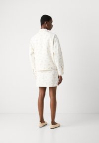 Veste et ensemble short à motif floral blanc, présentant une coupe décontractée, des manches longues et une texture douce, associés à des chaussures beige à enfiler.