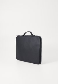 Czarna skórzana torba na laptopa o gładkiej fakturze, prostokątnym kształcie i z wbudowanym uchwytem. Posiada zamek błyskawiczny oraz minimalistyczny design.