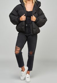 Chaqueta de plumas negra con capucha, puños elásticos y cierre de cremallera; combinada con jeans negros de cintura alta con desgastes en las rodillas y zapatillas blancas.
