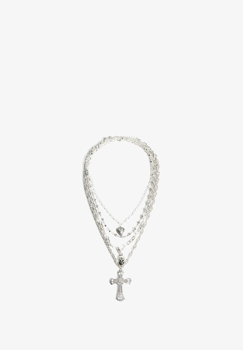 Srebrna ogrlica s več sloji in različnimi stili verig; vsebuje križni vis pendant, srčni obesek in akcent v obliki lobanje. Čist in svetleč zaključek.