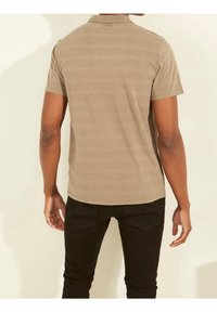 Polo beige à manches courtes avec une texture subtilement rayée, doté d'un col et d'un ourlet droit, associé à un jean noir ajusté.