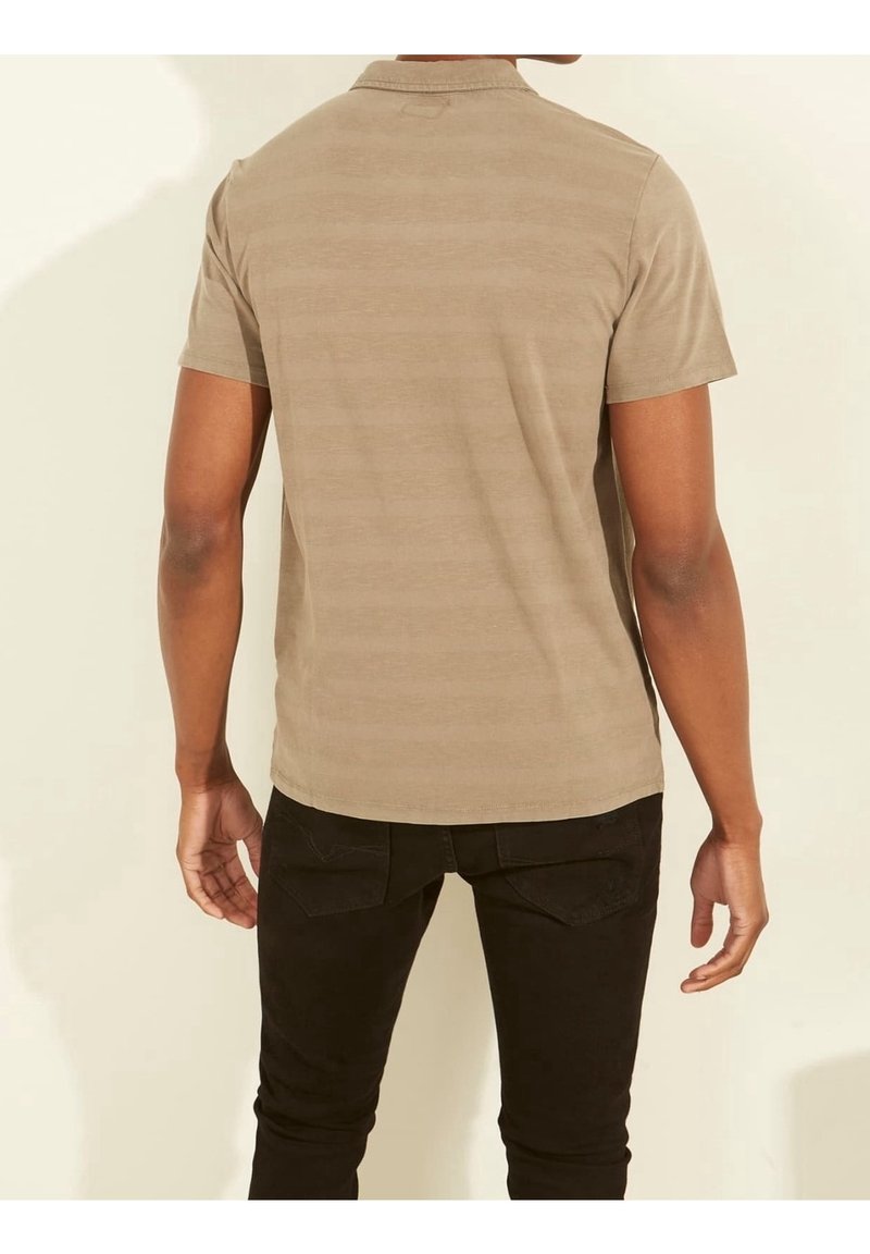 Polo beige à manches courtes avec une texture subtilement rayée, doté d'un col et d'un ourlet droit, associé à un jean noir ajusté.