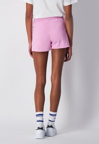 Růžové bavlněné kraťasy s elastickým pasem, hladkým povrchem a klasickým střihem, doplněné bílými botami a pruhovanými ponožkami.