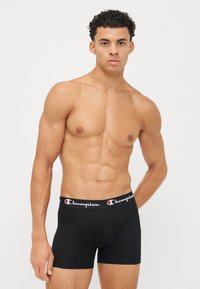 Black boxer briefs with a Champion logo waistband; soft, stretchy material; fitted design; mid-thigh length; smooth texture.