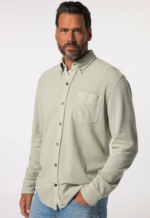 Camicia verde chiaro a maniche lunghe con bottoni, tasca sul petto, tessuto strutturato e bottoni metallici, abbinata a jeans azzurri.