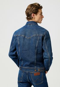 Takkipaita tummansinisestä denimestä, jossa on jämäkkä muotoilu. Siinä on klassisia ompeluyksityiskohtia ja brändätty nahkalappu takana.