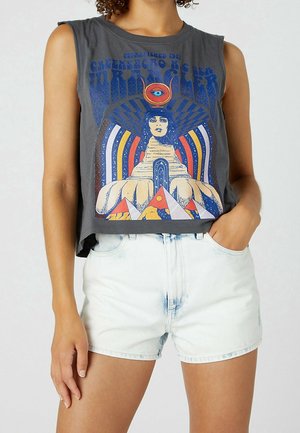 Top corto grigio senza maniche con design astratto colorato e testo, indossato con pantaloncini di jeans azzurri, mano del modello in tasca.