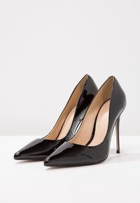 Svarta högklackade skor i lackläder med spetsig tå, elegant design och tunn stiletto-klack; insidan är försedd med en slät beige foder.