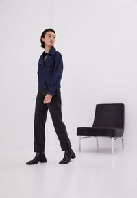 Jeansjacka i mörkblått med spridd krage och framfickor, matchad med svarta högmidjade byxor och svarta stövlar med fyrkantig klack.