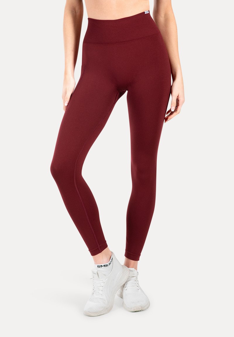 Leggings burdeos con una cinturilla alta, fabricados con un tejido elástico, que presentan una textura suave y un detallado de costuras mínimo. Combinados con zapatillas blancas.