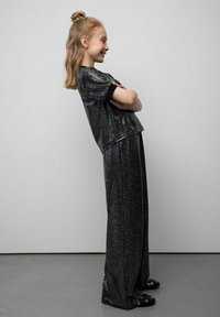 Czarny, cekinowy krótki top z krótkimi rękawami, zestawiony z wysokim stanem spodniami z czarnych cekinów. Obuwie to czarne chodaki z ozdobnymi elementami metalowymi.