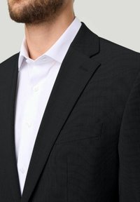 Schwarzer strukturierter Blazer mit einer einzelnen Brusttasche, kombiniert mit einem weißen Hemd mit Knopfleiste, das einen Spread-Kragen und sichtbare Knöpfe aufweist.