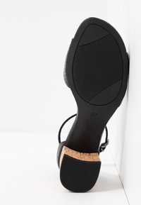 Sandale noire avec tige texturée, talon en liège et semelle en caoutchouc. Dispose de brides réglables et la pointure 37 est indiquée sur la semelle.