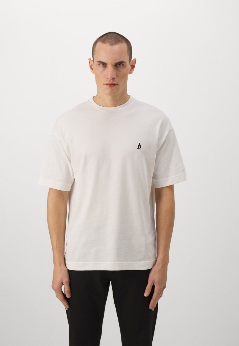 Tricou alb din bumbac, cu decolteu rotund, mâneci scurte și un mic logo negru pe partea stângă a pieptului. Croială ușor largă și textură netedă.