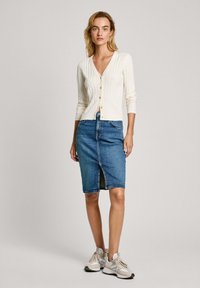 Biely rebrovaný cardigan s gombíkmi, skombinovaný s modrou džínsovou ceruzkovou sukňou s predným rozparkom a svetlými teniskami.