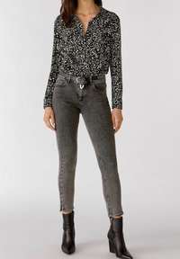Schwarz-weiße Leopardenmuster-Bluse mit Kragen, kombiniert mit grauen Skinny-Jeans und schwarzen Ankle-Boots mit seitlichen Reißverschlüssen.