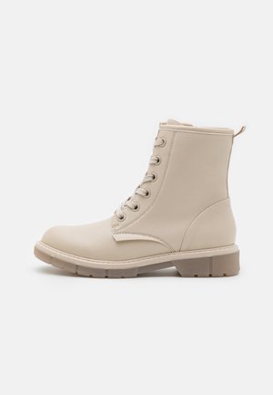 Bottine beige à lacets avec semelle épaisse et languette à l'arrière, conçue pour un usage décontracté ou en plein air.